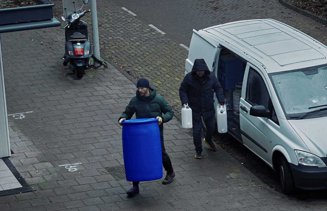 De nieuwe campagne Vreemd of Verdacht? roept iedereen op om alert te zijn tegen ondermijning. Op deze foto uit de campagne zie je mensen een blauw vat uit ene busje halen.