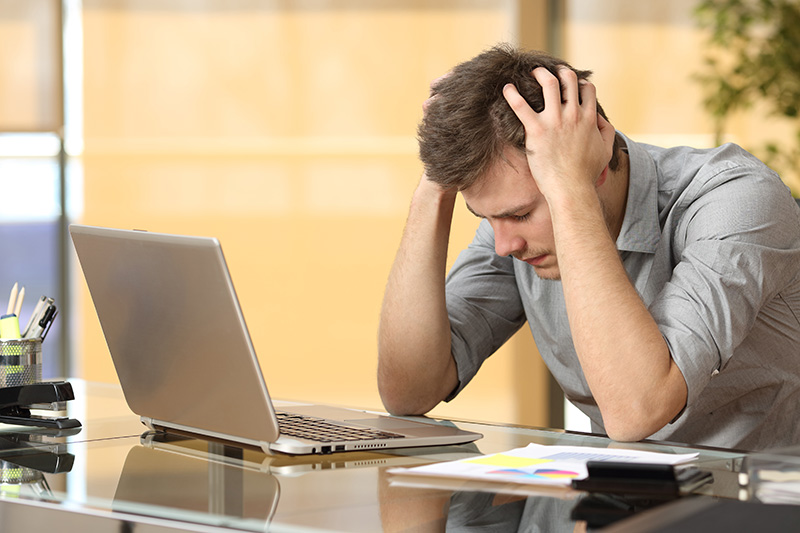 Man voorovergebogen met handen in het haar voor zijn laptop.