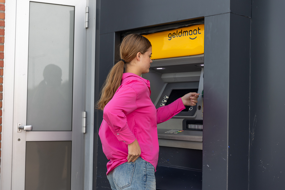 Tienermeisje pint geld bij een geldautomaat