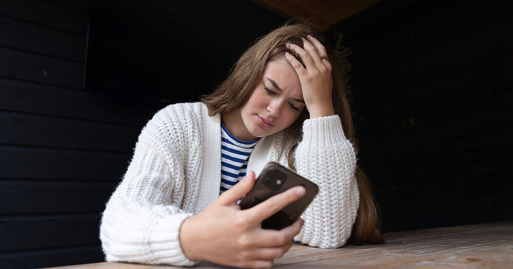 Meisje kijkt bezorgd op haar telefoon en zit met andere hand in het haar.